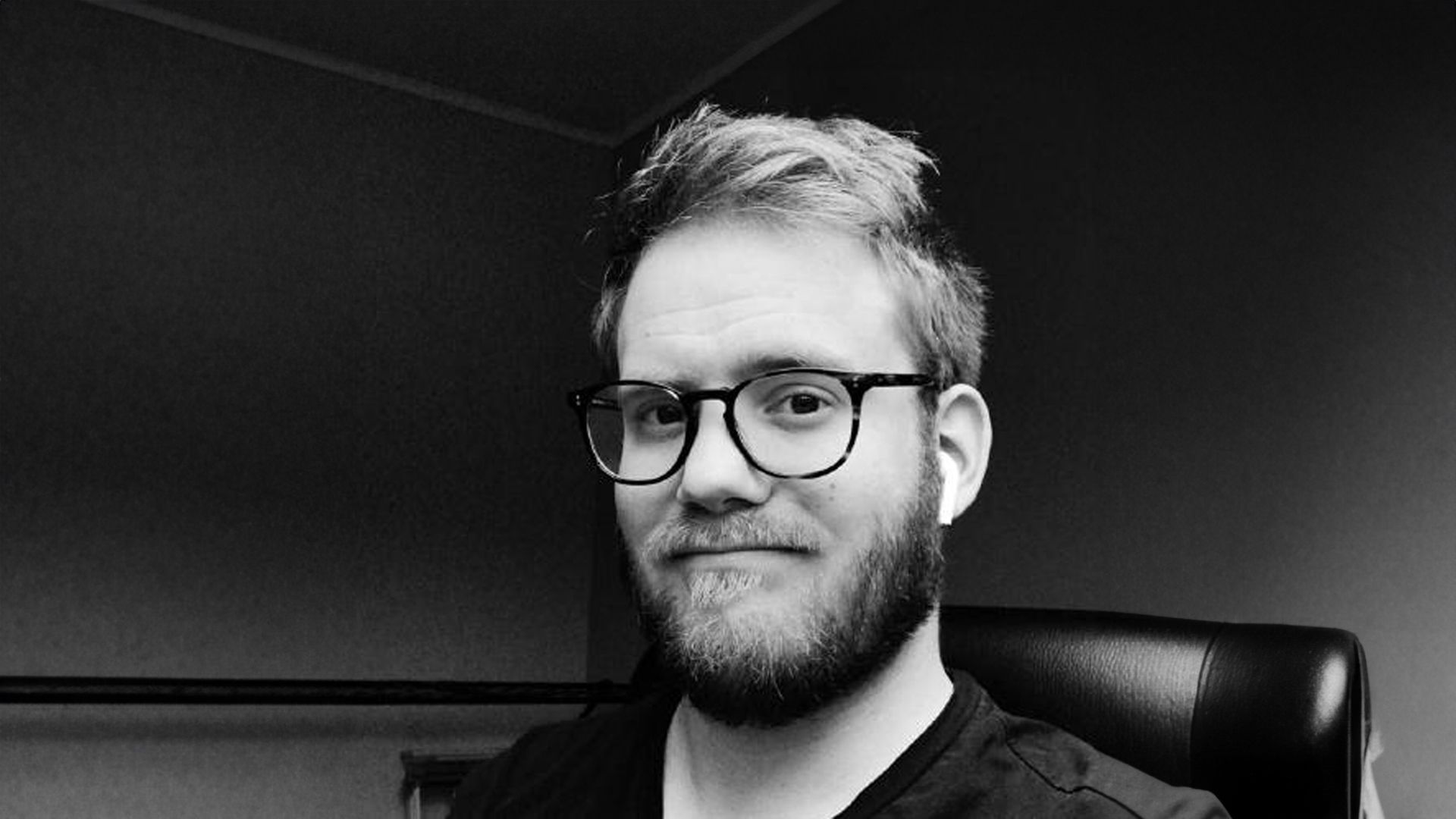 Black and white portrait of Kjetil Golid in glasses, seated in a dark office chair